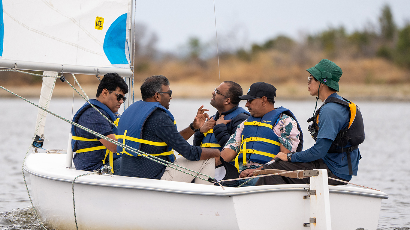 A group of men having a private sailing lesson. A group of men in a sailing boat having a private lesson on shoreline lake.