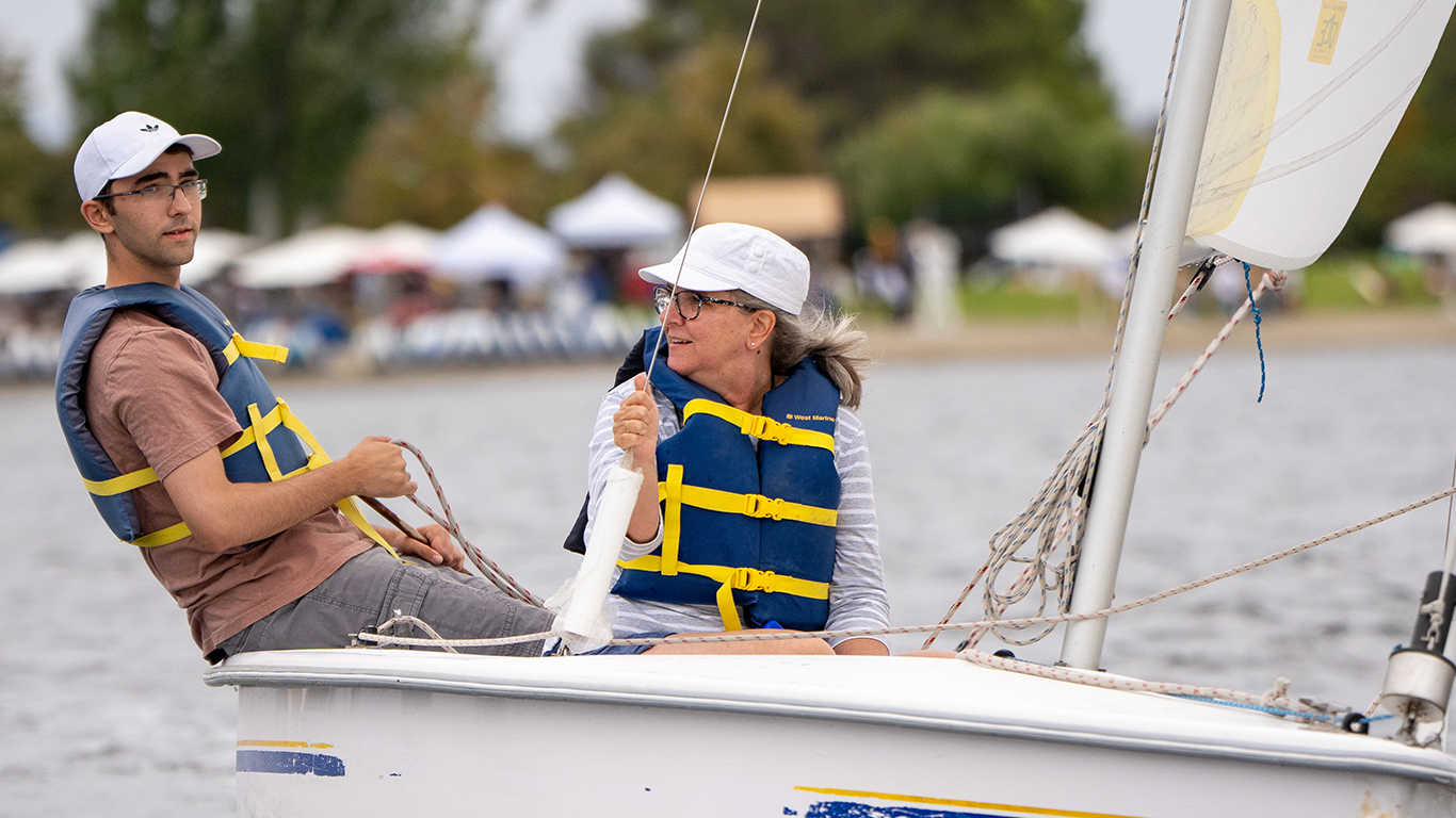 Two people in a sailboat on shoreline lake. Two people in a sailboat on shoreline lake.
